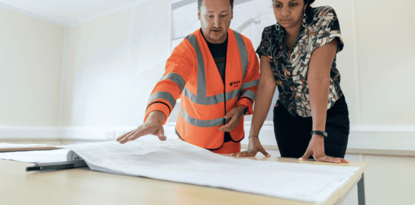 construction worker and woman standing over and reviewing architectural plans