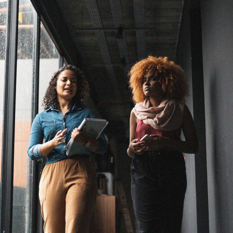 Two women in conversation walking in business office hallway