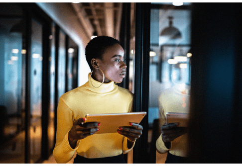 Contemplative woman with an ipad looking into a conference room with the glow reflecting on her face.