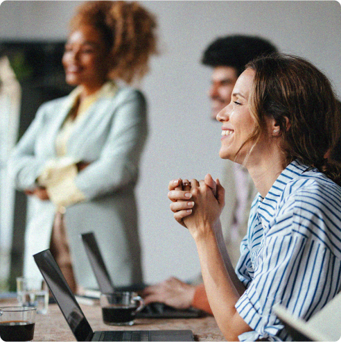 Woman in meeting with laptop smiling while watching a presentation and people in the background