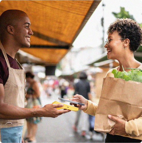 Two smiling people completing a transaction of grocery goods outdoors