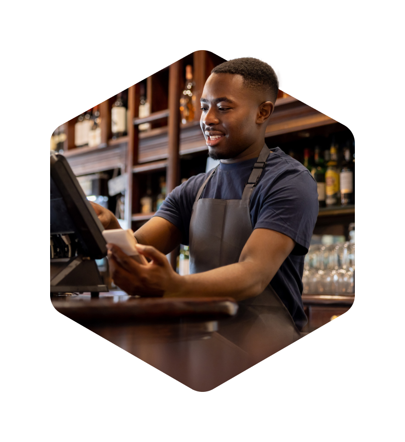 A photo masked in a hexagon of a male worker on a register inputting information and smiling.