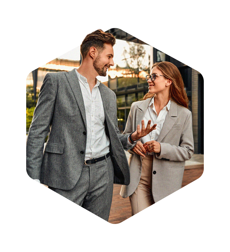 A warm photo masked in a hexagon a man and woman in suits having a dynamic conversation outdoors