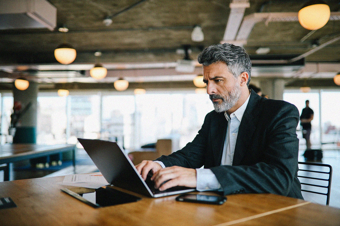 Man with beard in suit focusing in open floor plan office on a laptop