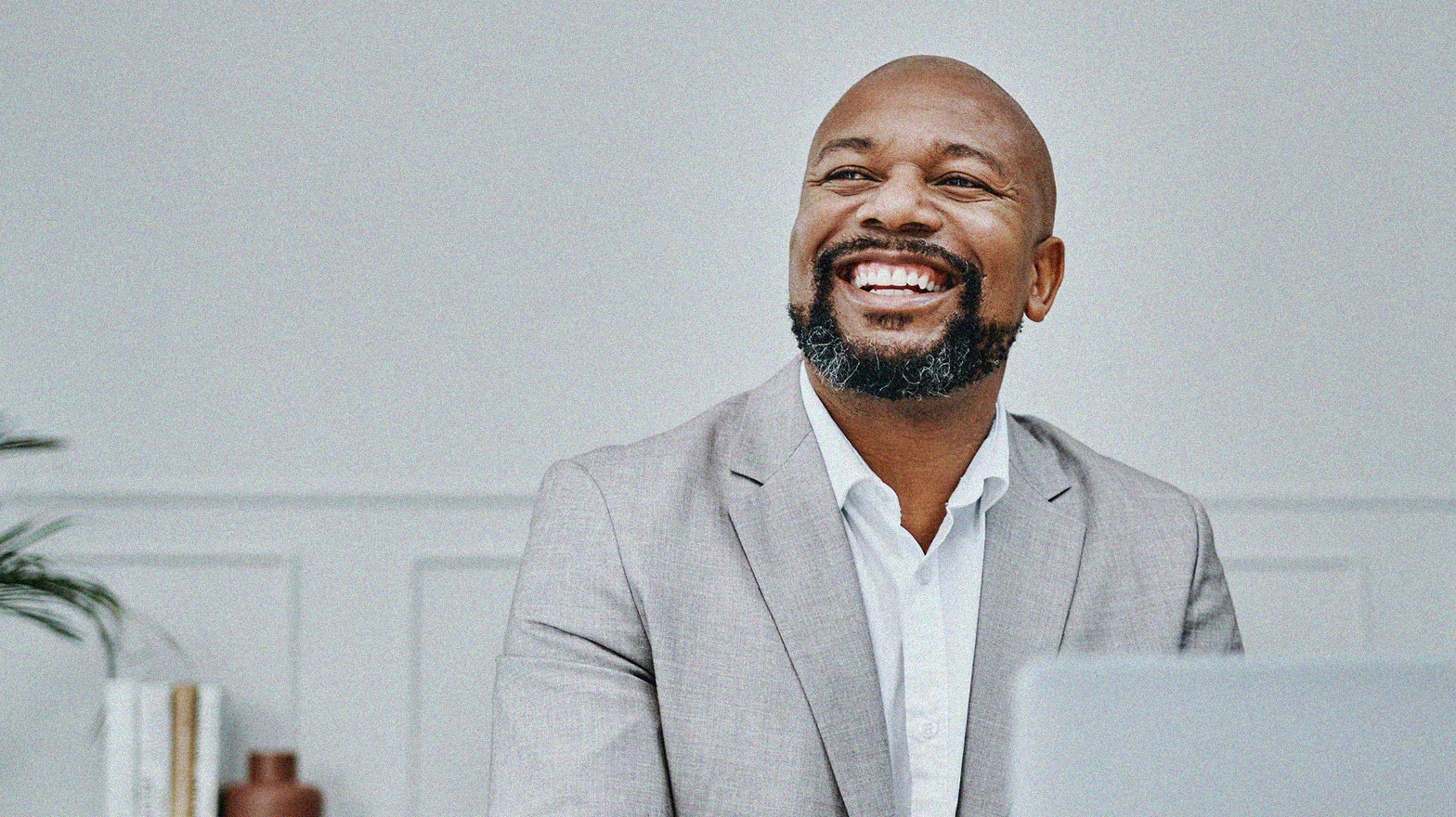 Business professional smiling man at desk behind a computer in monochrome white room