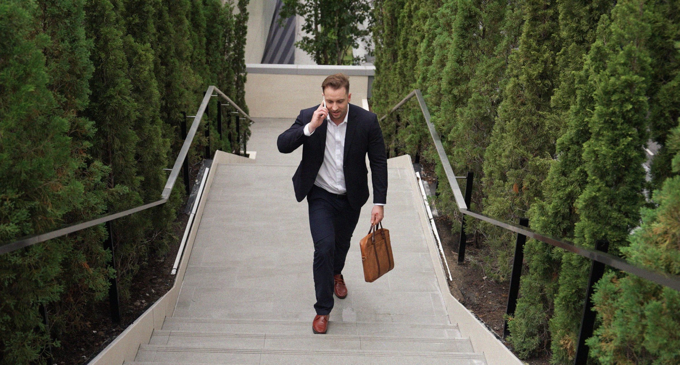 Man in suit on phone walking up stairs outdoors holding a leather briefcase