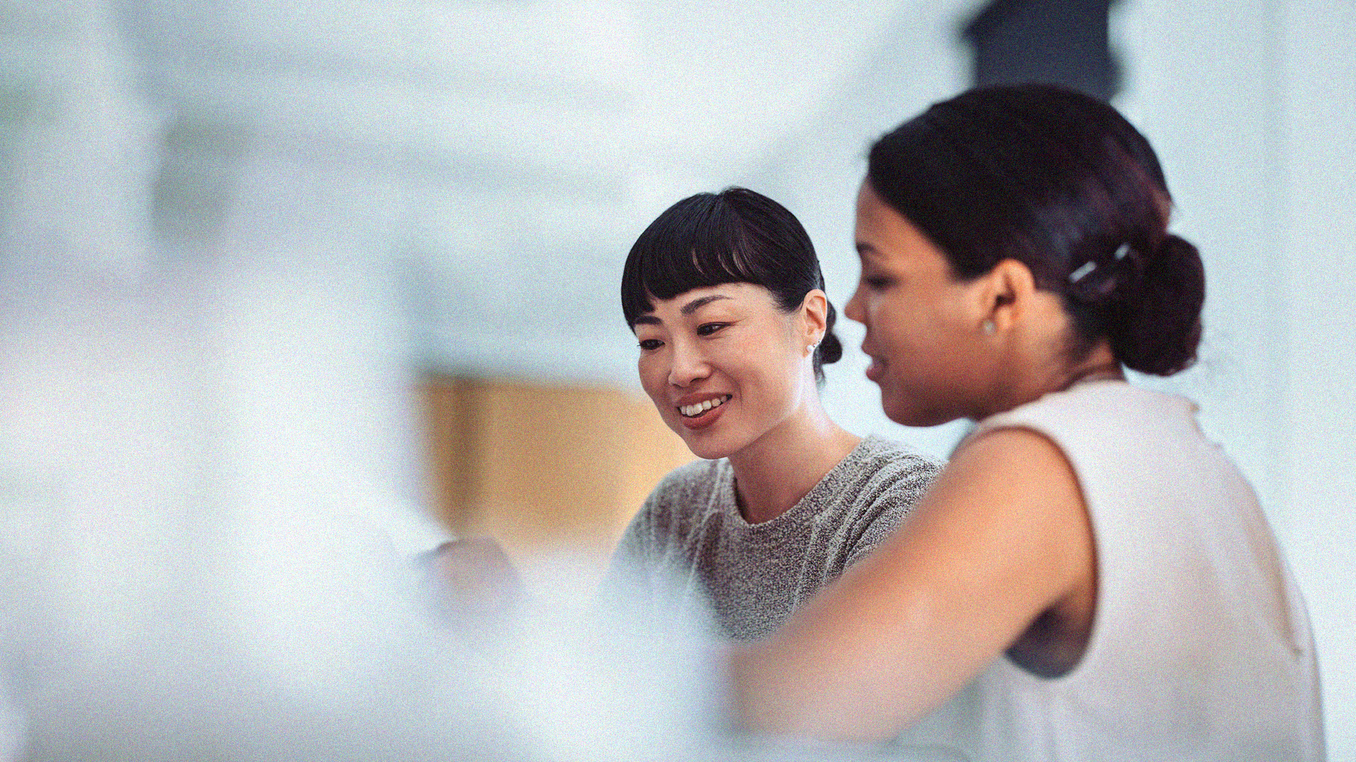 Two women smiling and discussing information that is blurred by an object in the foreground