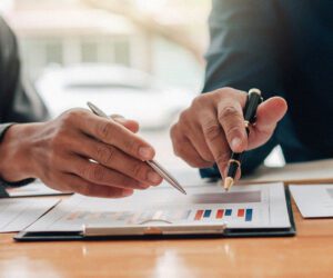 Two business professionals discussing financial charts and analyzing cash flow strategies with pens in hand, representing steps to accelerate cash flow in business.