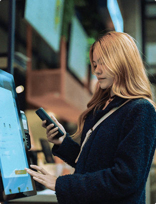 Woman holding cellphone in front of a tablet screen