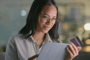 Smiling woman with glasses making an online payment on a tablet while holding a credit card.