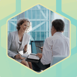 Two business professionals sitting in an office talking by a laptop and notebook