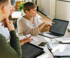 Business team collaborating as one member points to financial data displayed on a laptop screen.