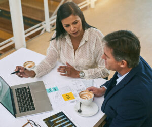 Business colleagues reviewing charts and notes during a meeting, with a laptop and coffee on the table.