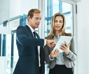 Business professionals reviewing data on a tablet in a modern office, with one person pointing at the screen while discussing information.