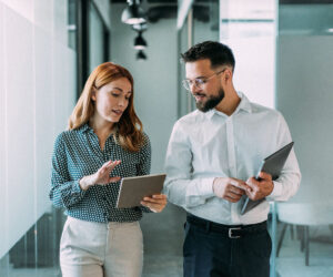 Two business professionals reviewing information on a tablet while walking through a modern office.