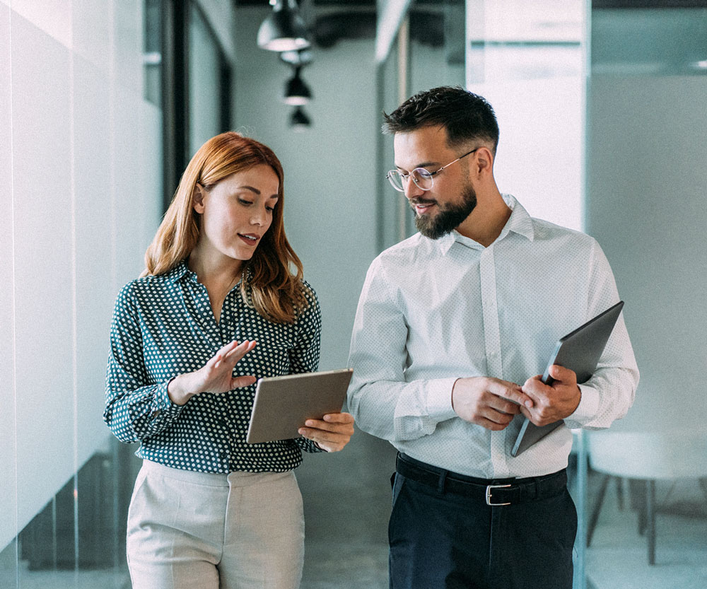 Two business professionals reviewing information on a tablet while walking through a modern office.