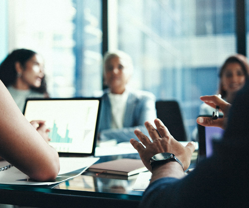 Finance team discussing performance data displayed on a laptop during a meeting.