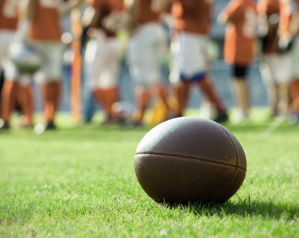 Football on the field with college players blurred in the background.